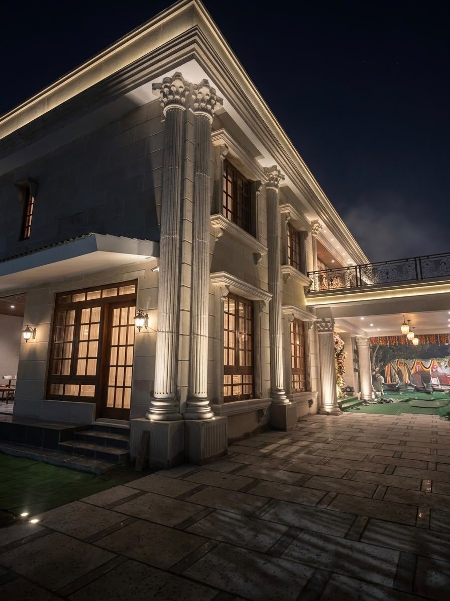 Stone façade of a private residence in Hyderabad at night, with fluted columns and lit window surrounds