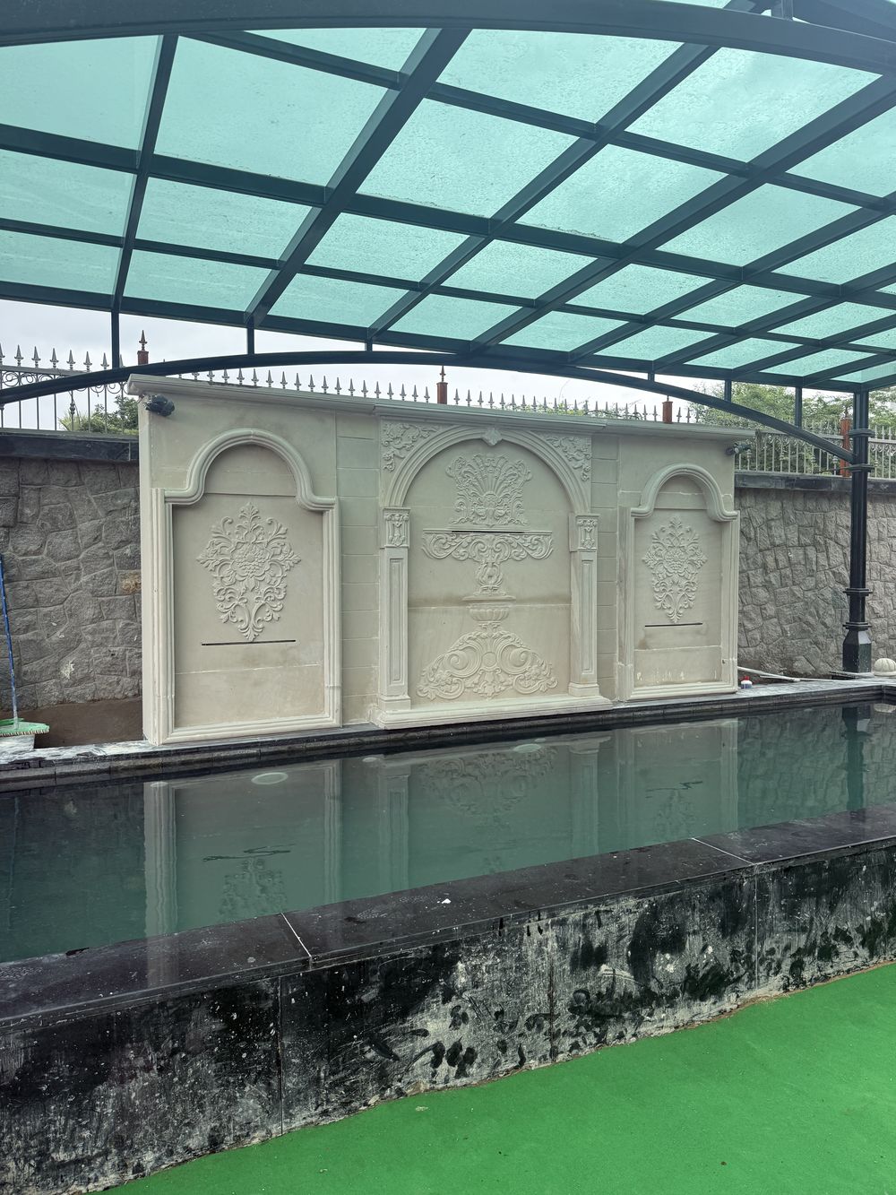 Carved stone wall feature with arched panels above the pool