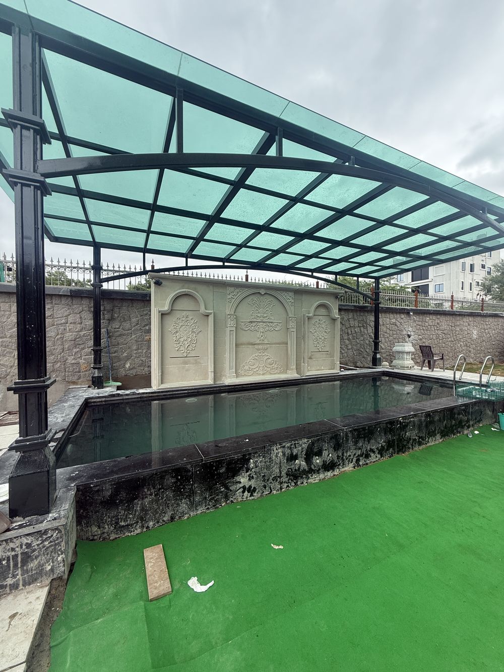 Pool with a carved stone wall feature under a glass canopy